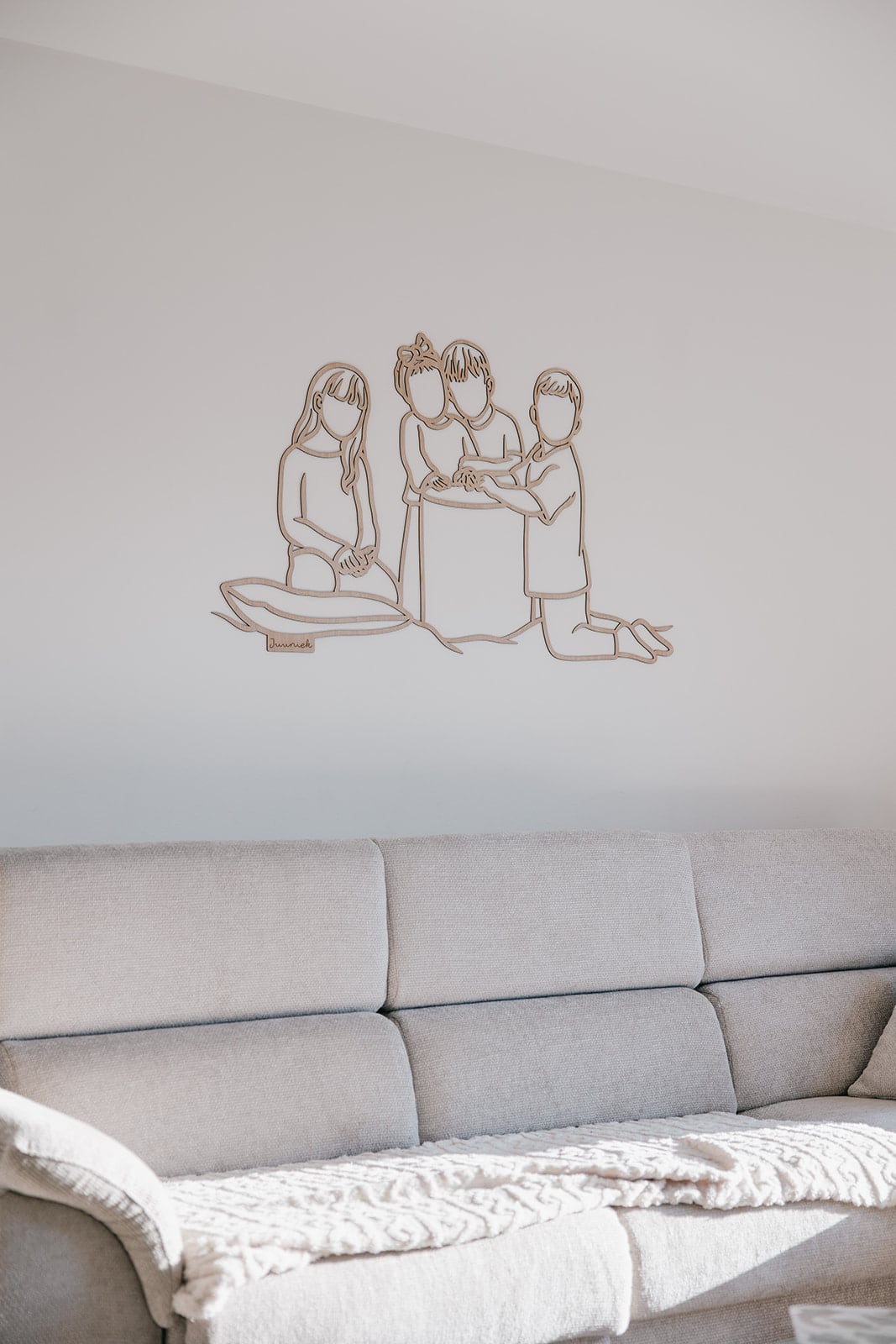Linienporträt aus Holz von vier Kindern über einem hellen Sofa