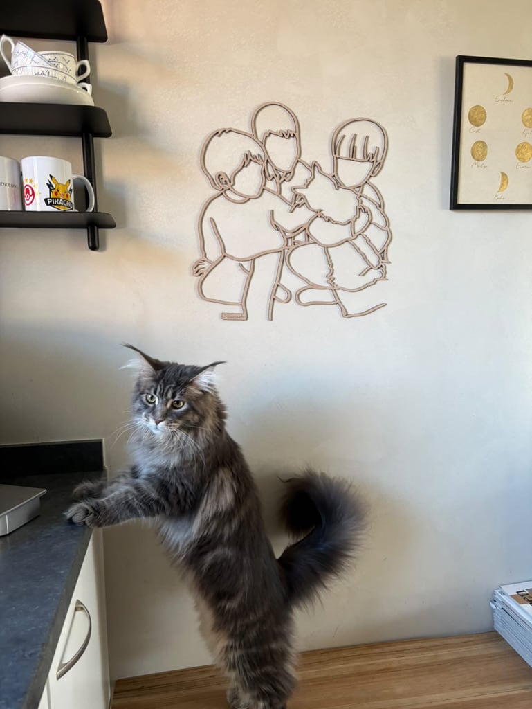 Maine Coon steht aufrecht unter einem Linienporträt aus Holz der Kinder mit ihrer Katze, in der Küche